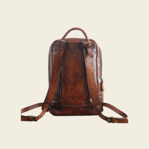 Back of the leather travel backpack showing padded shoulder straps and top handle, cream background