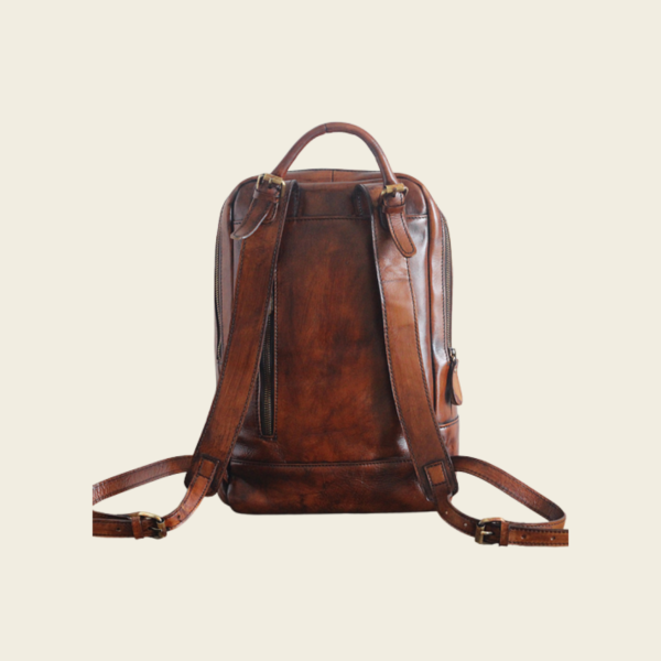 Back of the leather travel backpack showing padded shoulder straps and top handle, cream background